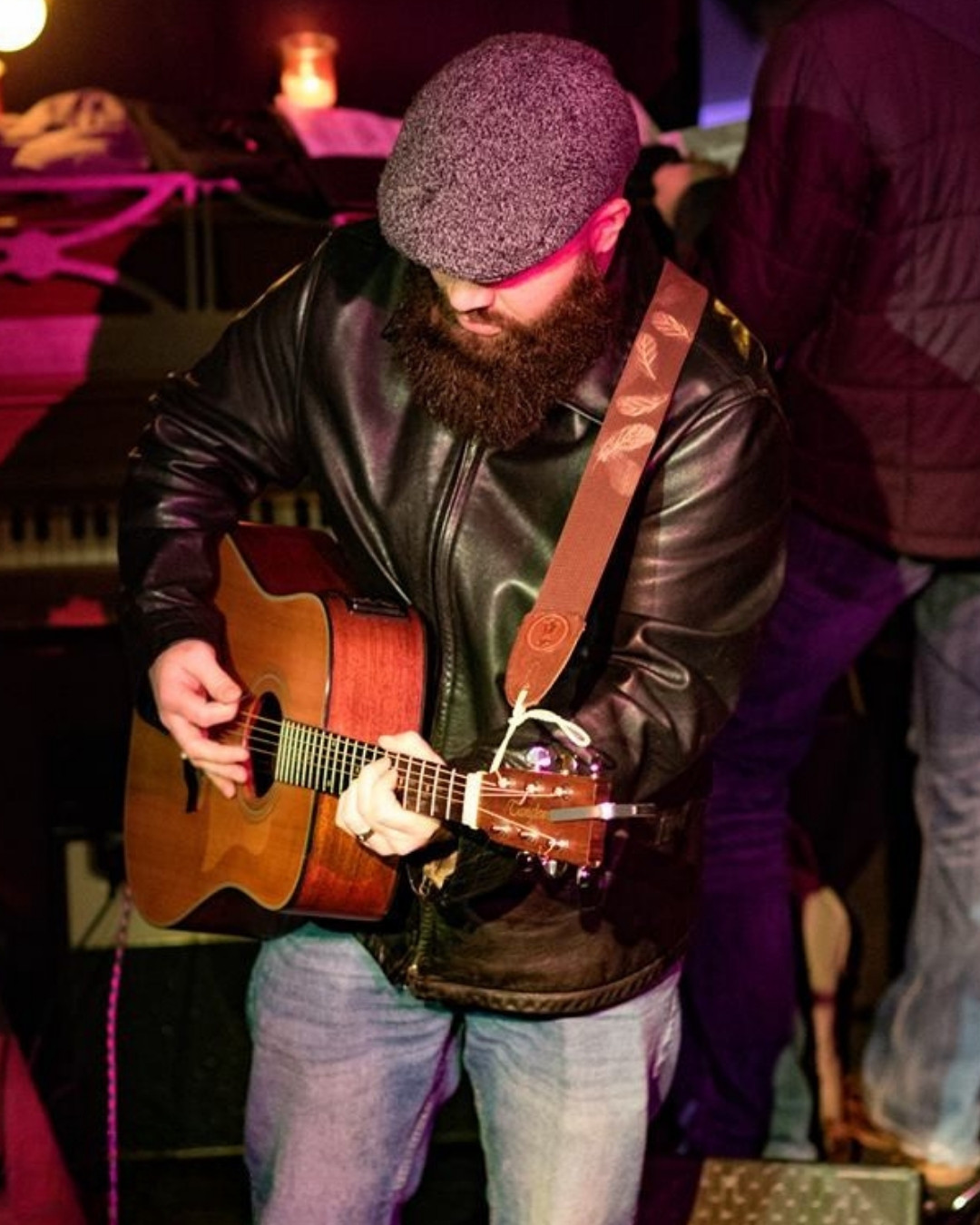 Caleb Taylor playing acoustic guitar under purple stage light